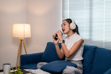 Fototapeta premium A woman is sitting on a blue couch, playing a video game and holding a cup