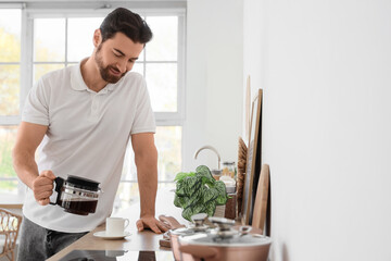 Morning of handsome man pouring coffee into cup in kitchen