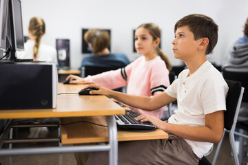 Pre-adolescent children learn to work at a computer in a school classroom