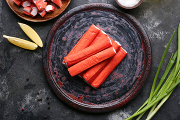 Plate with tasty crab sticks, slices of lemon and green onion on black background © Pixel-Shot