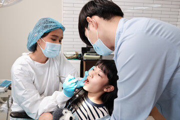 Asian female pediatric dentist examines a girl's teeth in dental clinic and takes care and encourages of father, mouth oral hygiene, and professional orthodontic healthcare work in a kid hospital.