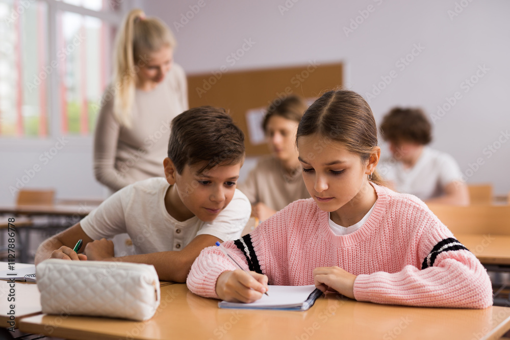 Wall mural Portrait of teenage school girl and boy sitting together in classroom during lesson in secondary school