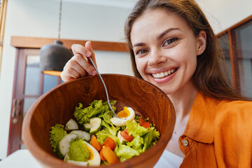Young woman smiling while holding a fresh salad bowl in a bright kitchen, showcasing healthy eating habits and vibrant colors