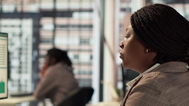 Focused african american general manager multitasking at desk to solve business tasks and operations on computer and documents. Woman meeting deadlines while making strategic decisions. Camera A.