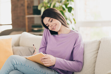 Obraz premium Photo of attractive young teen woman write notebook talk phone call dressed purple outfit bright cozy day light home interior living room