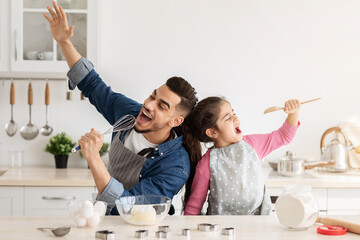Cheerful arab father and little daughter having fun while baking together in kitchen, happy middle...