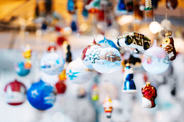 Variety of hand-painted Christmas ornaments, including baubles and figurines, hang from strings in festive market setting, beautifully lit by warm lights