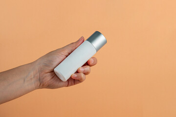  White glass cosmetic bottle in hand, Skin care or sunscreen cosmetic on cream background.