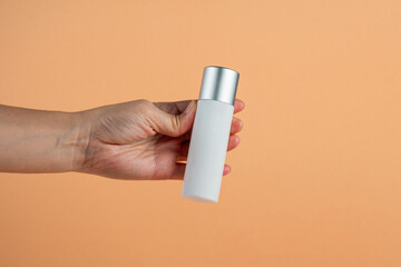  White glass cosmetic bottle in hand, Skin care or sunscreen cosmetic on cream background.