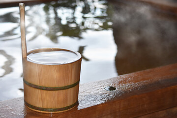 湯気が立ち昇る檜の露天風呂に置かれた檜の手桶　湯船の反射する景色 © skyhigh.ring