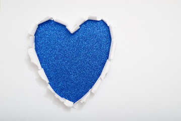 Heart-shaped hole torn on white paper revealing a blue glitter background.