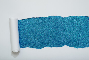 Obraz premium Torn white paper revealing a blue glitter background.