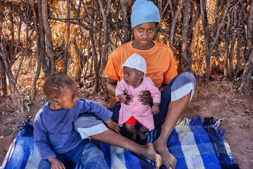 poverty in the village, african family mother and kids on a blanket in the shade at home, charity...