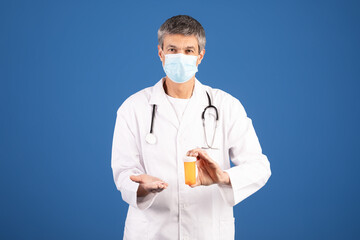 A Caucasian doctor in his 50s wears a mask and holds a prescription bottle in one hand while extending the other hand slightly. The backdrop is a solid blue, emphasizing his healthcare role.