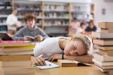 Portrait of a tired fifteen-year-old schoolgirl lying on a desk among textbooks in the school...