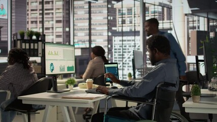 African american male worker in wheelchair trying to solve daily tasks at the office, examining organizational data and working on a forecasting plan. Man with impairment ensures analysis. Camera B.
