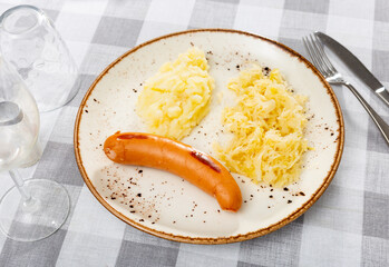 Appetizing fried meat sausages with potatoes and sauerkraut served on platter
