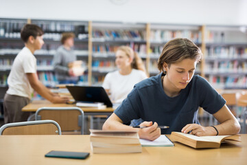 Fifteen-year-old schoolboy studying in the library writes an synopsis from a textbook