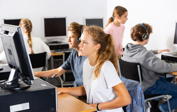 Portrait of a fifteen-year-old schoolgirl studying at a computer in a class at an informatics lesson with classmates