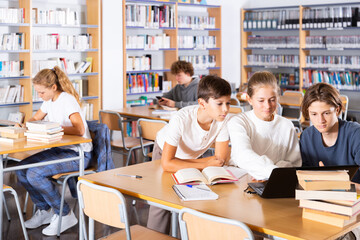 Group of schoolchildren reading books together in library and preparing for the school exam