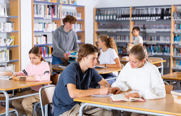 Schoolchildren doing their homework in the school library write out a synopsis from the textbook in...