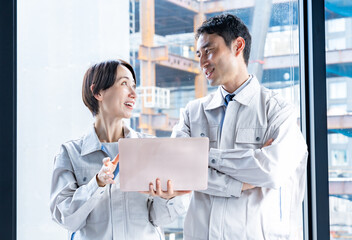 工事現場をバックにパソコンを見ながら話す男女