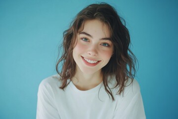 Fototapeta premium Portrait of a beautiful young woman in a white t-shirt against a blue background.