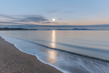Obraz premium Serene beach at sunrise with calm waters and distant hills.
