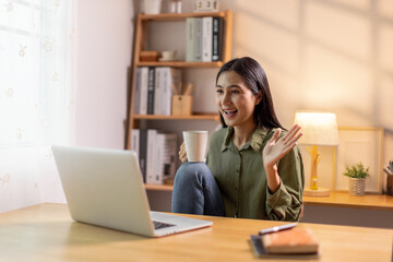 Beautiful young Asian woman working with laptop computer in home kitchen. Work at home. Remote studying E-learning, Watching online education, Webinar at house
