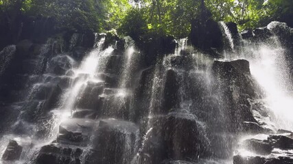 Establishing pan right of Kanto Lampo Waterfall surrounded by tropical plants and cascading rocks, Bali, Indonesia