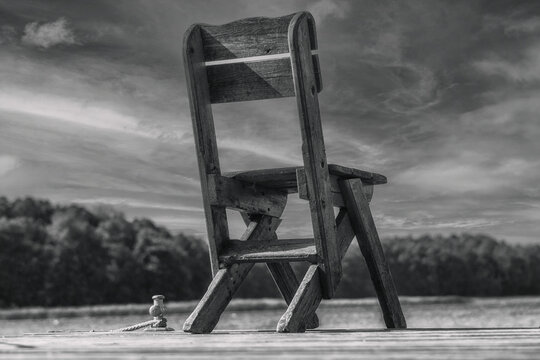 A lonely wooden chair stands abandoned on an old boat dock by the water in midsummer.
Idyllic solitude in paradise. Fishing chair by the lake.