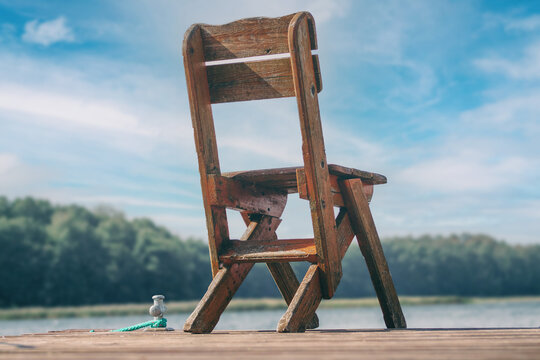 A lonely wooden chair stands abandoned on an old boat dock by the water in midsummer.
Idyllic solitude in paradise. Fishing chair by the lake.