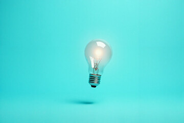 A minimalist image of a glowing light bulb floating against a turquoise background, symbolizing ideas, innovation, and creativity