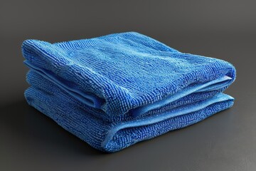 A stack of neatly folded blue microfiber cloths on a dark surface