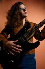 Young female musician playing electric guitar on orange background