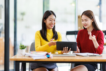 Obraz premium Shot of two businessasianwomen working together on digital tablet. Creative female executives meeting in an office using tablet pc and smiling. 