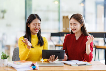 Shot of two businessasianwomen working together on digital tablet. Creative female executives meeting in an office using tablet pc and smiling.
