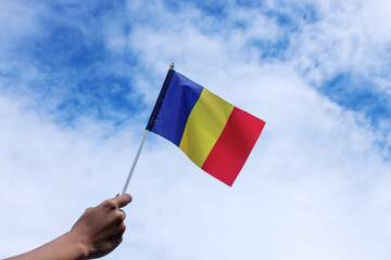 Raised Hands Holding Rumania National Flag Waving in Beautiful Clouds.
