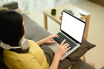 Fototapeta premium Overhead view of young woman typing on a laptop while sitting on couch