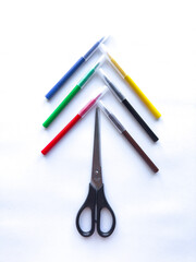 Colorful pens arranged around scissors in creative geometric pattern