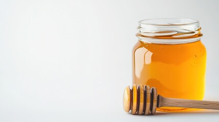 glass jar of golden honey with wooden dipper resting beside it on seamless white background