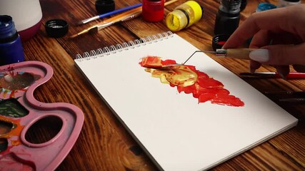 Girl hand paints with a stainless steel spatula with gouache colors in a notebook