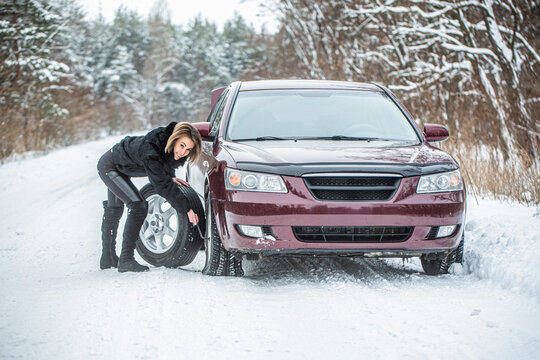 Woman changing the punctured tyre on his car in winter. Fault car in the winter. Girl trying to repair the car, engine repair, tire change. Female using changing wheel