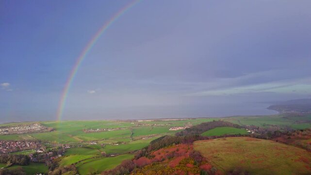 Aerial shot flying over Exmoor National park with huge rainbow in the sky