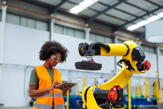 Female industrial engineer programming robotic arm in factory