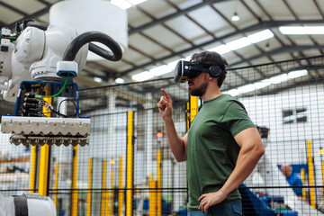 Engineer using virtual reality headset controlling robotic arm in factory