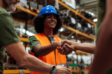 Smiling female engineer shaking hands with colleagues in warehouse