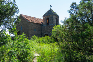 The small church on the hill among bushes and trees is part of the Shio-Mgvime monastery. The bright blue sky in the background.