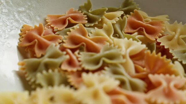 Closeup of colorful farfalle pasta with red, green, and yellow hues shot in a bowl under soft lighting that accentuates its texture and vibrant colors