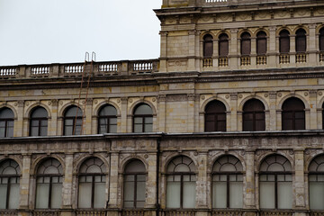 Historic Building Facade Featuring Arches Windows and a Ladder on a Cloudy Day in an Urban Setting